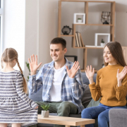 Pai e mãe surdos ensinando o filho com as mãos para o alto e sua filha observando os ensinamentos